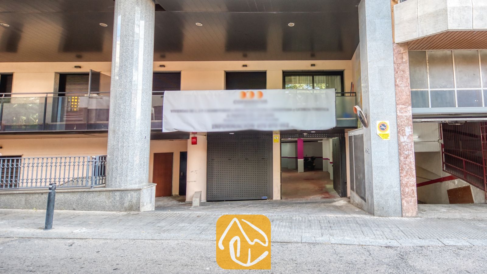 Vakantievilla's Costa Brava Spanje - Apartment Gaudi - Buitenaanzicht van het gebouw van Apartment Gaudi met stenen pilaren, balkons met glazen balustrades en een garage-ingang met een banner.