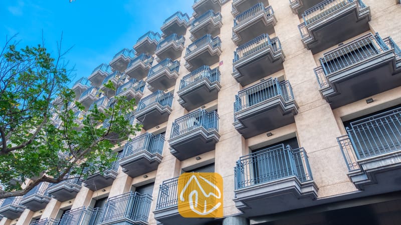 Vakantievilla's Costa Brava Spanje - Apartment Dali - Buitengevel van Appartement Dali met rijen balkons met donkere balustrades tegen een beige muur onder een helderblauwe hemel