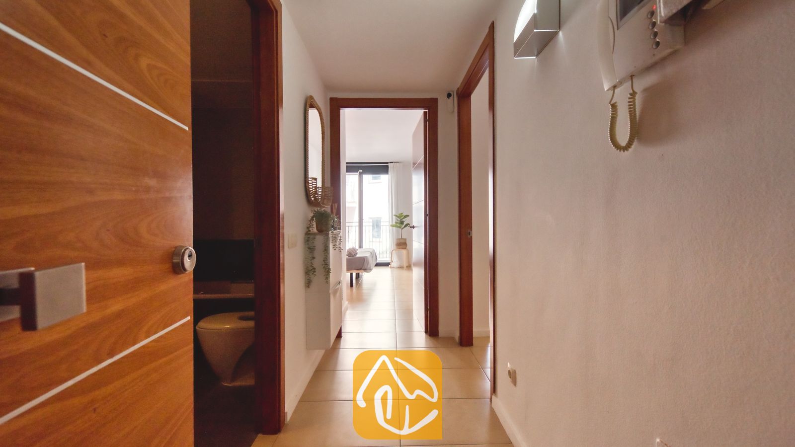 Vakantievilla's Costa Brava Spanje - Apartment Dali - Binnenhal met lichte tegelvloer, witte muren en houten deurposten die toegang bieden tot de verschillende kamers van Appartement Dali.
