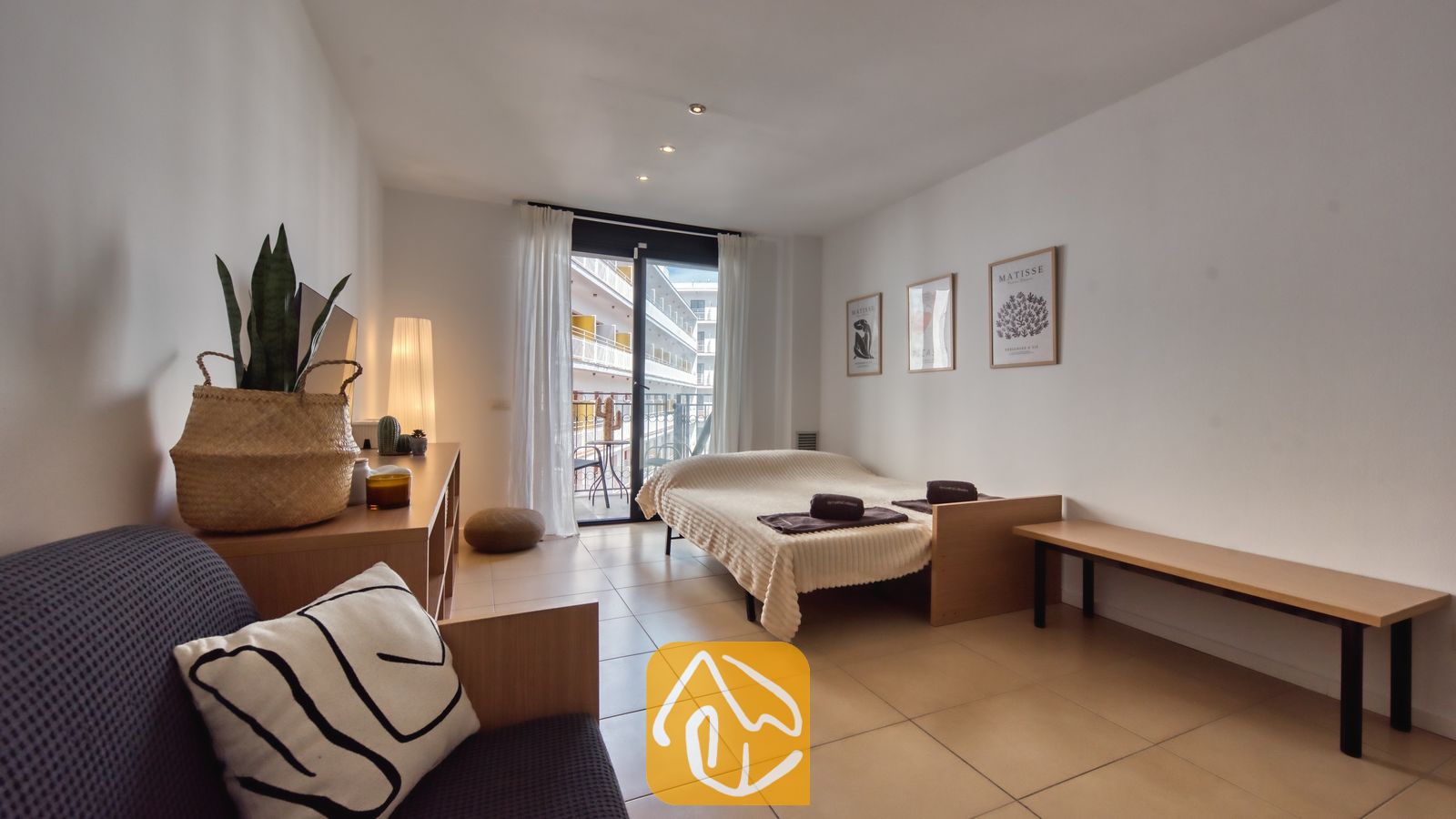 Vakantievilla's Costa Brava Spanje - Apartment Dali - Slaapkamer in Appartement Dali met een eenpersoonsbed met een neutrale sprei, witte glasgordijnen, tegelvloeren, ingelijste wanddecoratie en een glazen deur die uitkomt op een balkon.