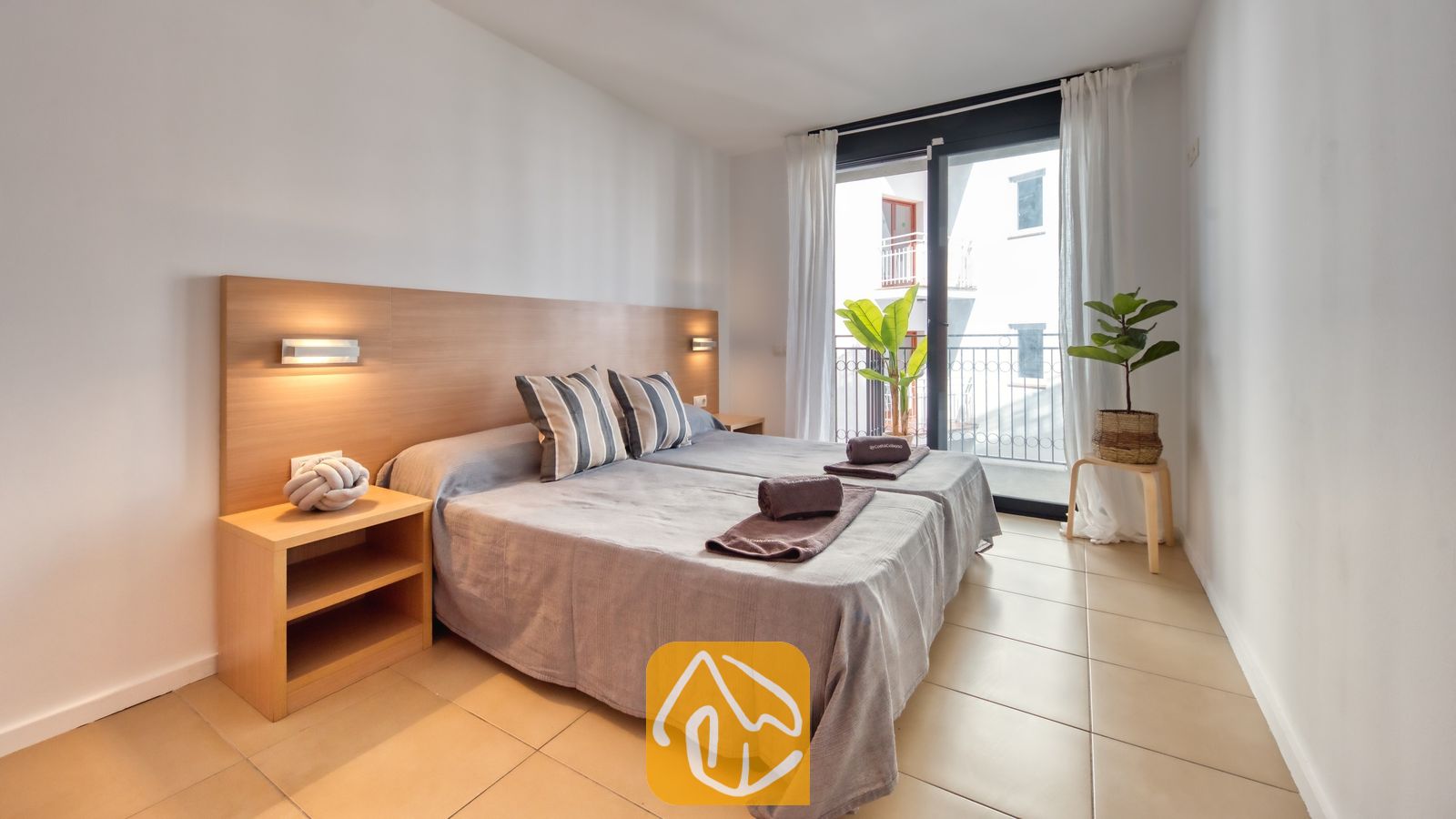 Vakantievilla's Costa Brava Spanje - Apartment Dali - Slaapkamer in Appartement Dali met een tweepersoonsbed voorzien van grijs beddengoed, gestreepte kussens en een houten hoofdbord met ingebouwde verlichting dat toegang biedt tot een balkon.