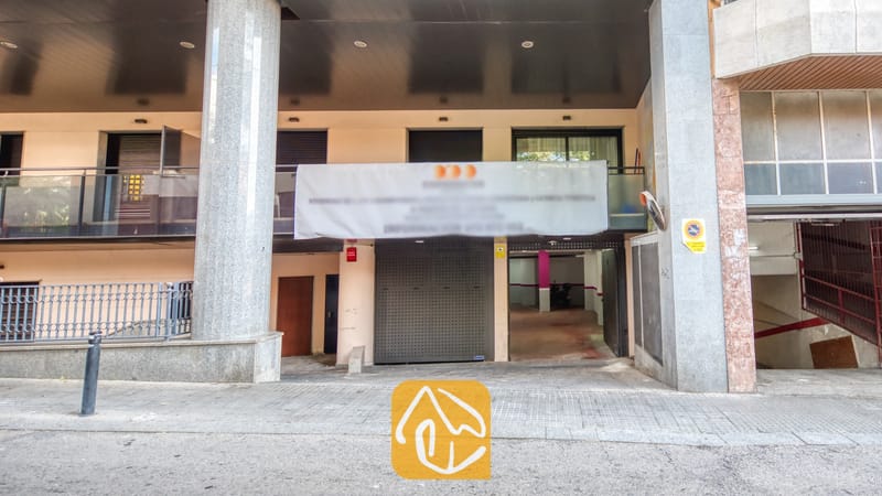 Vakantievilla's Costa Brava Spanje - Apartment Dali - Buitengevel van Appartement Dali met een overdekte parkeerinrit, grote stenen zuilen en balkons met metalen hekken boven de begane grond.