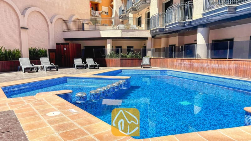 Vakantievilla's Costa Brava Spanje - Apartment Dali - Buitenzwembad met blauwe mozaïektegels en ligstoelen bij Apartment Dali, omringd door appartementengebouwen met meerdere verdiepingen en balkons.