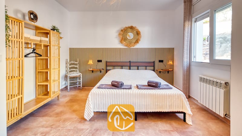 Villas de vacances Costa Brava Espagne - Villa Ibiza - Chambre avec un lit double orné de serviettes roulées, tête de lit à lattes en bois, armoire en bambou et sol carrelé.