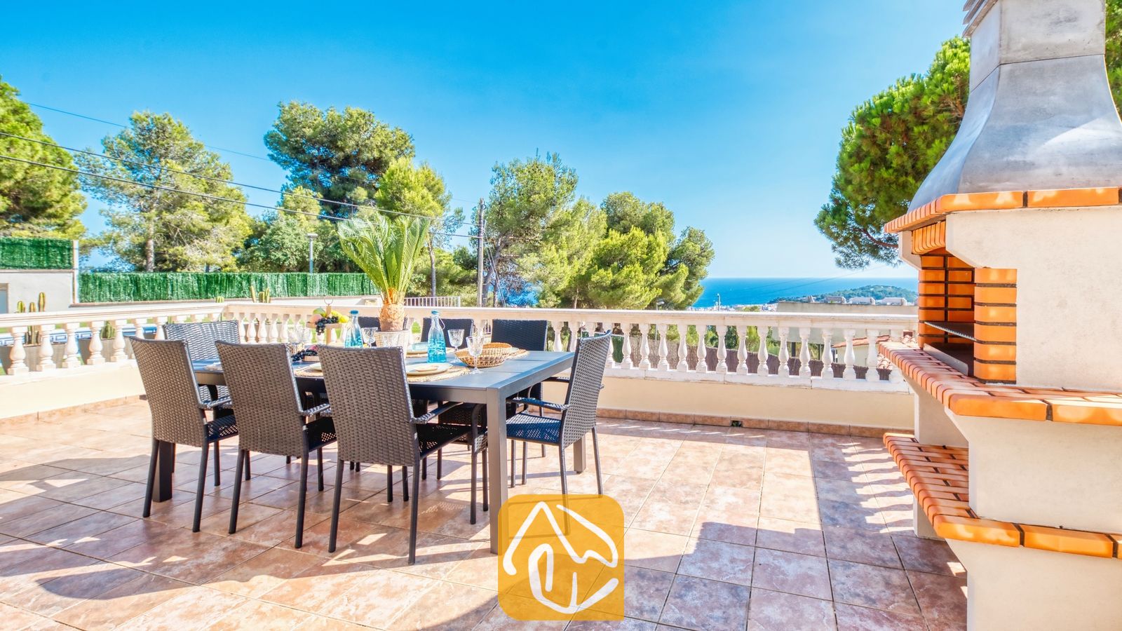 Vakantievilla's Costa Brava Spanje - Villa Ibiza - Terras van Villa Ibiza met een eettafel buiten en zwarte Wicker stoelen, een aangesloten stenen barbecue en uitzicht op zee.