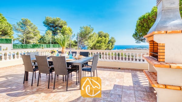 Vakantievilla's Costa Brava Spanje - Villa Ibiza - Terras van Villa Ibiza met een eettafel buiten en zwarte Wicker stoelen, een aangesloten stenen barbecue en uitzicht op zee.