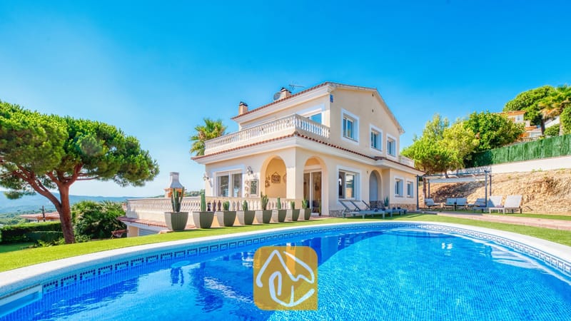 Vakantievilla's Costa Brava Spanje - Villa Ibiza - Privézwembad op de voorgrond met Villa Ibiza, een crèmekleurig huis van twee verdiepingen, een groen gazon en cactussen in potten onder een helderblauwe hemel.