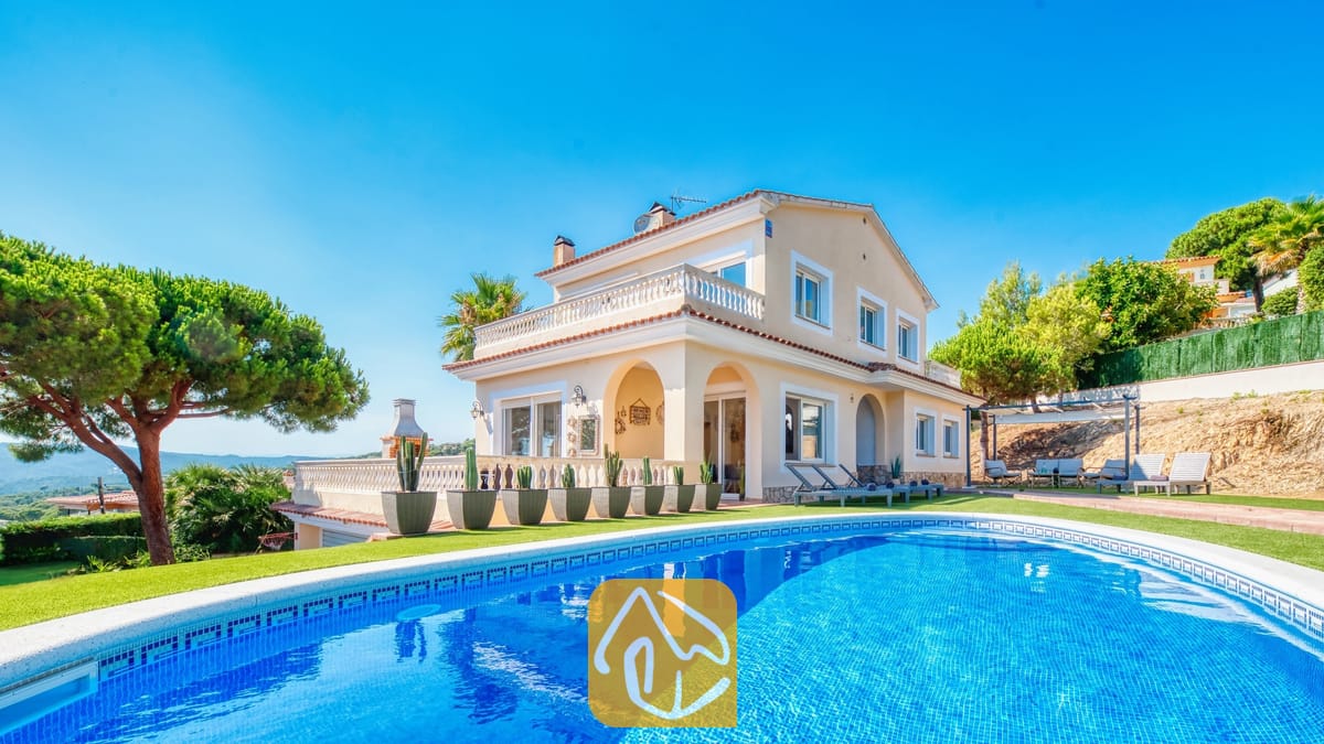Vakantievilla's Costa Brava Spanje - Villa Ibiza - Privézwembad op de voorgrond met Villa Ibiza, een crèmekleurig huis van twee verdiepingen, een groen gazon en cactussen in potten onder een helderblauwe hemel.