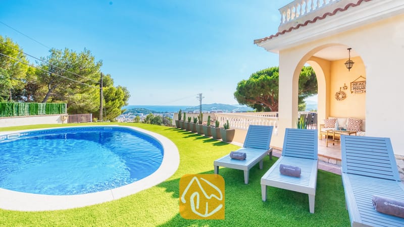 Vakantievilla's Costa Brava Spanje - Villa Ibiza - Privézwembad en blauwe houten ligstoelen op kunstgras bij Villa Ibiza met uitzicht op de verre zee en bomen.