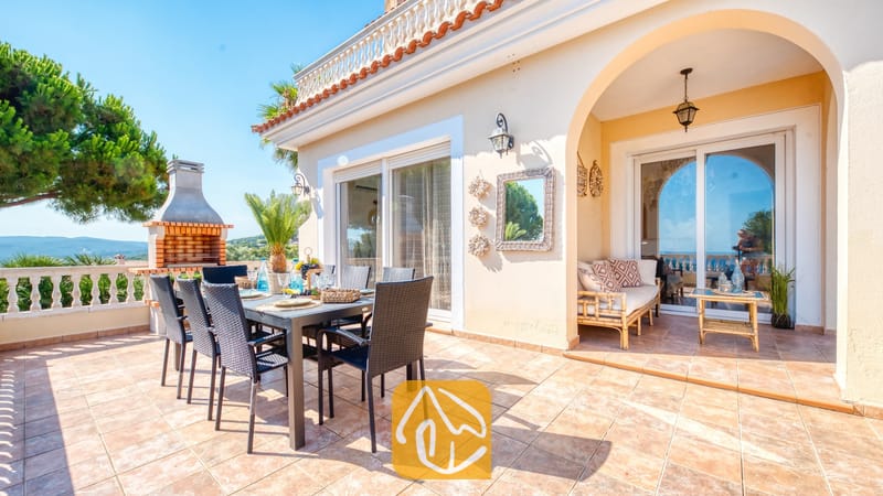 Vakantievilla's Costa Brava Spanje - Villa Ibiza - Buitenterras van Villa Ibiza met een eettafel, zwarte stoelen, een stenen barbecue en een overdekte zithoek onder een toogboog.