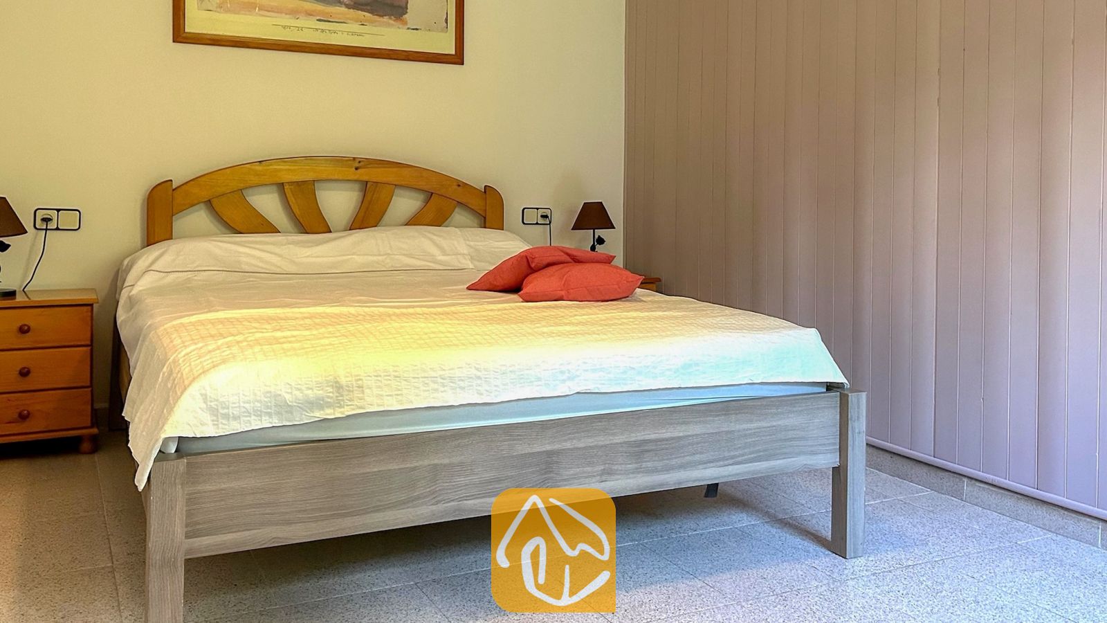 Vakantievilla's Costa Brava Spanje - Villa Iako - Slaapkamer met een tweepersoonsbed met een houten hoofdbord, wit beddengoed, rode kussens en bijpassende houten nachtkastjes op een tegelvloer.