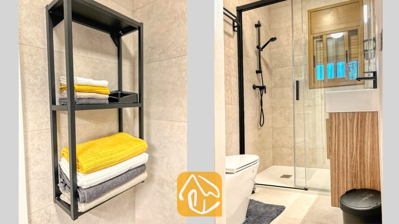 Villas de vacances Costa Brava Espagne - Villa Iako - Salle de bains moderne aux murs carrelés de beige, dotée d'une étagère en métal noir garnie de serviettes pliées, d'une douche à l'italienne à encadrement noir et d'un meuble sous-vasque en bois.