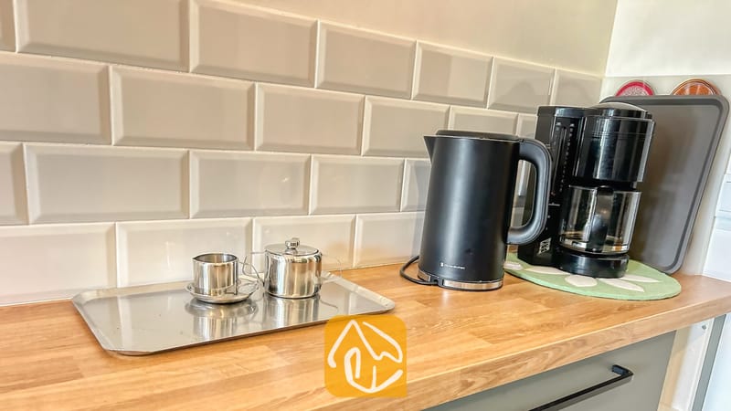 Villas de vacances Costa Brava Espagne - Villa Iako - Bouilloire électrique et cafetière noires sur un plan de travail en bois devant une crédence en carrelage beige, accompagnées d'un petit plateau argenté contenant des tasses en métal.