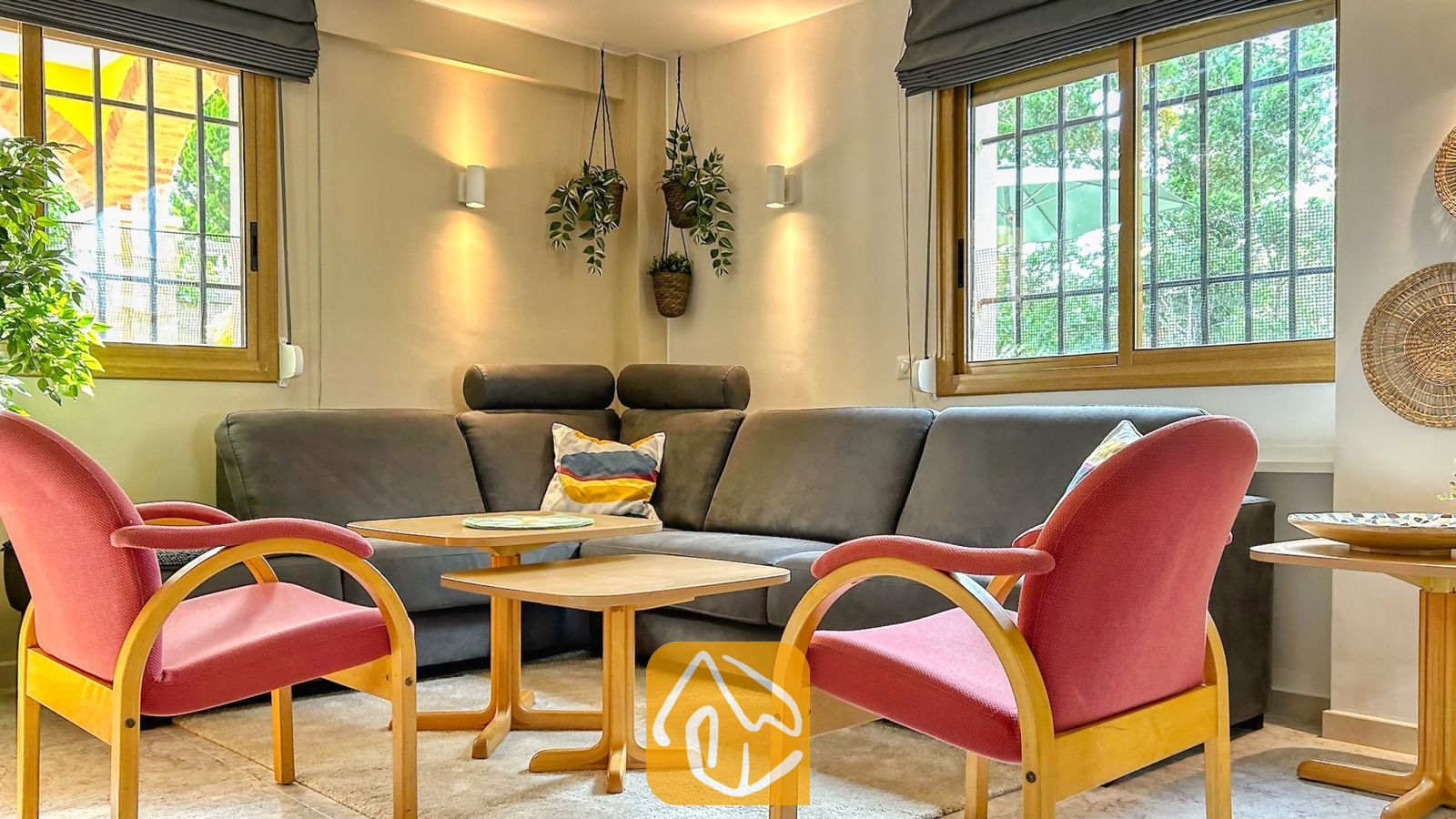 Vakantievilla's Costa Brava Spanje - Villa Iako - Zithoek in Villa Iako, voorzien van een grote grijze hoekbank, twee roze fauteuils met houten frames en twee kleine houten salontafels.