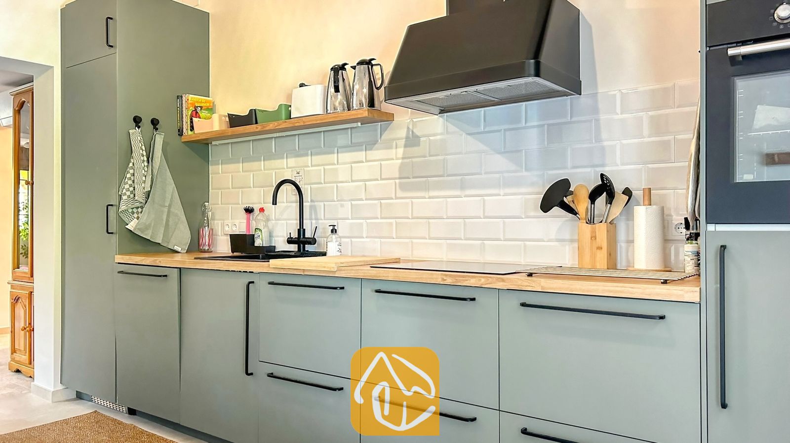 Vakantievilla's Costa Brava Spanje - Villa Iako - Moderne keuken met saliegroene keukenkastjes, houten aanrechtbladen en een witte metrotegelwand, voorzien van een zwarte kraan en afzuigkap.