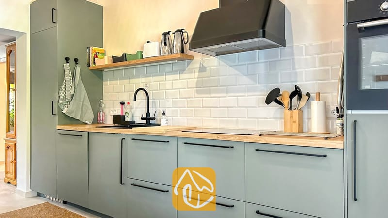 Villas de vacances Costa Brava Espagne - Villa Iako - Cuisine moderne dotée de meubles vert sauge, de plans de travail en bois et d'une crédence en carrelage métro blanc, agrémentée d'une robinetterie et d'une hotte aspirante noires.
