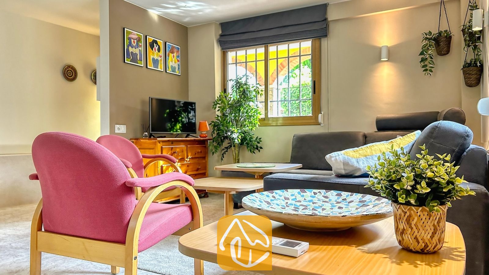 Vakantievilla's Costa Brava Spanje - Villa Iako - Woonkamer voorzien van een grijze hoekbank, roze fauteuils met houten frames en een houten salontafel met een decoratieve schaal.