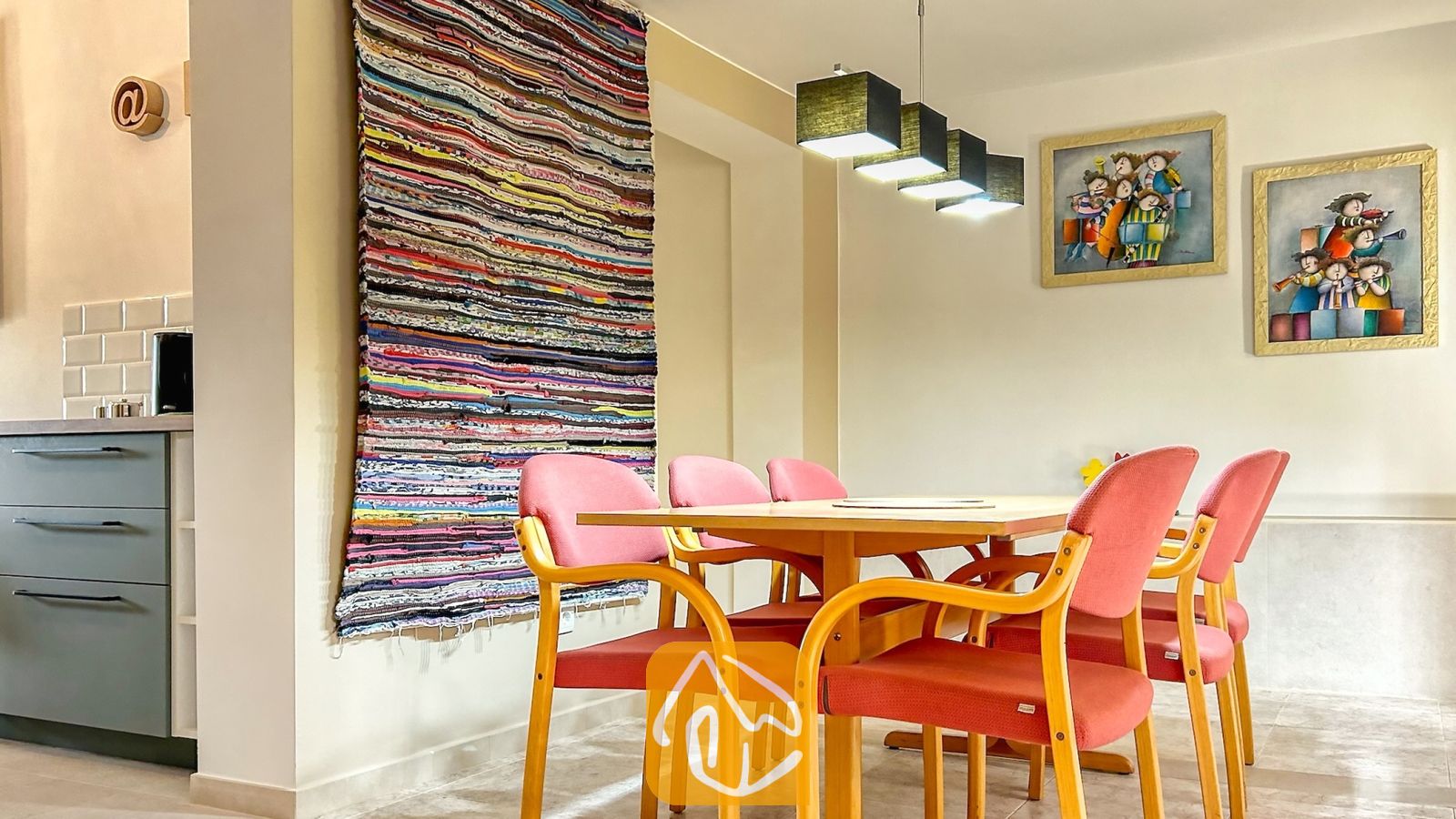 Vakantievilla's Costa Brava Spanje - Villa Iako - Eethetgedeelte met een houten tafel, omringd door roze gestoffeerde stoelen, verlicht door een rij vierkante hanglampen.