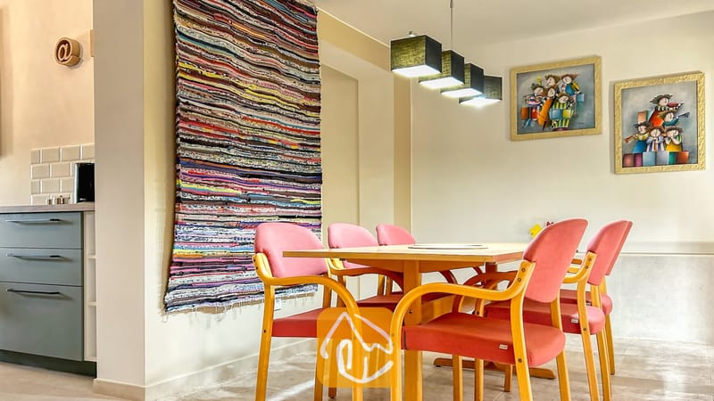 Villas de vacances Costa Brava Espagne - Villa Iako - Espace repas doté d'une table en bois entourée de chaises capitonnées roses, le tout éclairé par un alignement de suspensions carrées.
