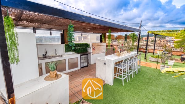 Villas de vacances Costa Brava Espagne - Villa Soleia - Cuisine et bar sur le toit de la Villa Soleia, dotés de comptoirs en béton blanc, d'une pergola en chaume, de tabourets de bar et d'un sol en gazon synthétique.
