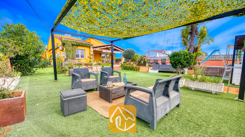 Villas de vacances Costa Brava Espagne - Villa Soleia - Espace salon extérieur à la Villa Soleia, comprenant des fauteuils en osier foncé, un canapé assorti et une table basse, installés sous une toile d'ombrage jaune sur une pelouse verdoyante.