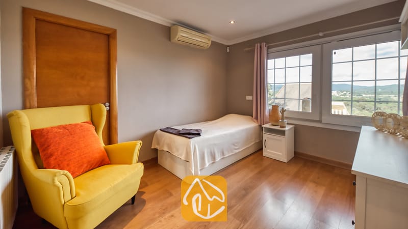 Villas de vacances Costa Brava Espagne - Villa Soleia - Chambre avec parquet comprenant un lit simple, un fauteuil jaune vif agrémenté d'un coussin orange, ainsi qu'une fenêtre offrant une vue sur l'extérieur.