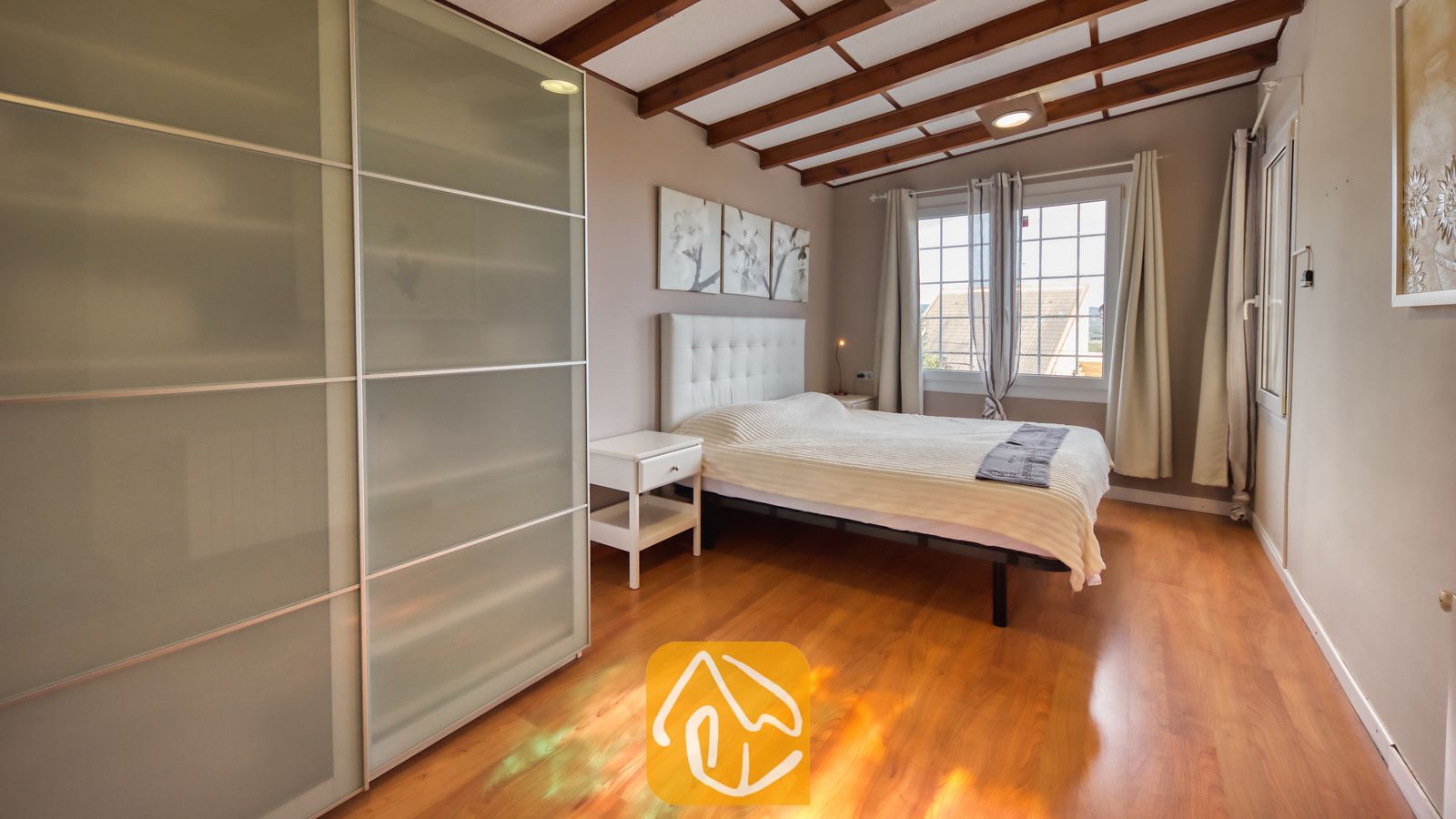 Villas de vacances Costa Brava Espagne - Villa Soleia - Chambre avec un lit double, poutres apparentes au plafond, portes de placard en verre dépoli et parquets en bois.