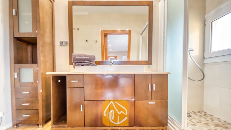 Villas de vacances Costa Brava Espagne - Villa Soleia - Meuble de salle de bain moderne avec un meuble vasque en bois foncé, un grand miroir rectangulaire et des serviettes pliées sur la vasque blanche.