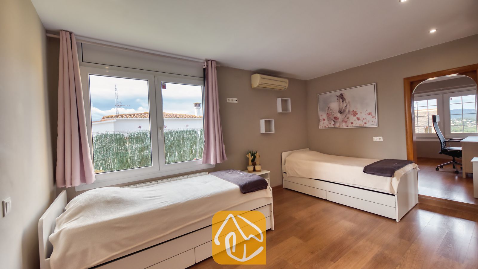 Villas de vacances Costa Brava Espagne - Villa Soleia - Chambre à lits jumeaux avec deux lits simples blancs, parquet, rideaux roses encadrant une fenêtre et peinture de cheval sur le mur beige.