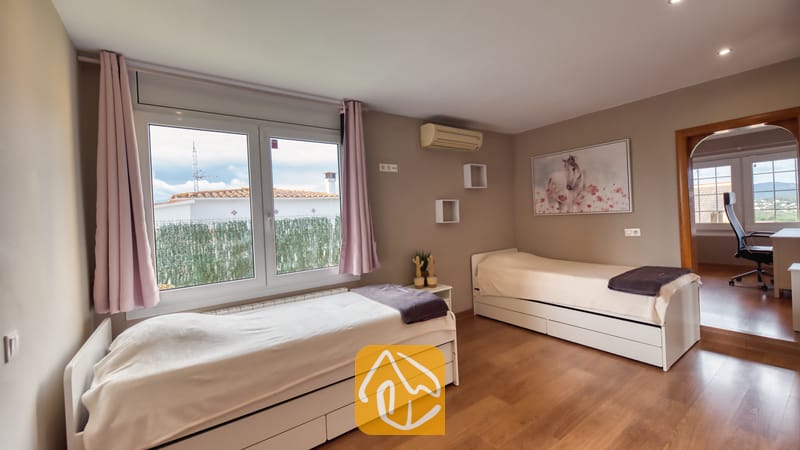 Villas de vacances Costa Brava Espagne - Villa Soleia - Chambre à lits jumeaux avec deux lits simples blancs, parquet, rideaux roses encadrant une fenêtre et peinture de cheval sur le mur beige.