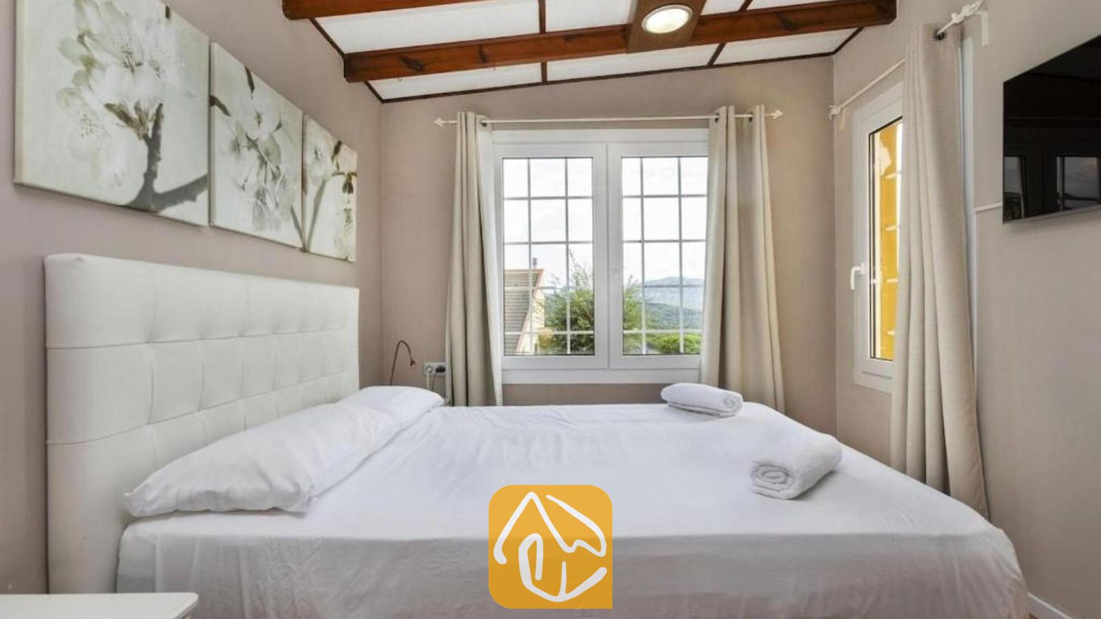Vakantievilla's Costa Brava Spanje - Villa Soleia - Slaapkamer met een wit getuft hoofdbord, zichtbare houten plafondbalken en een raam met uitzicht naar buiten.