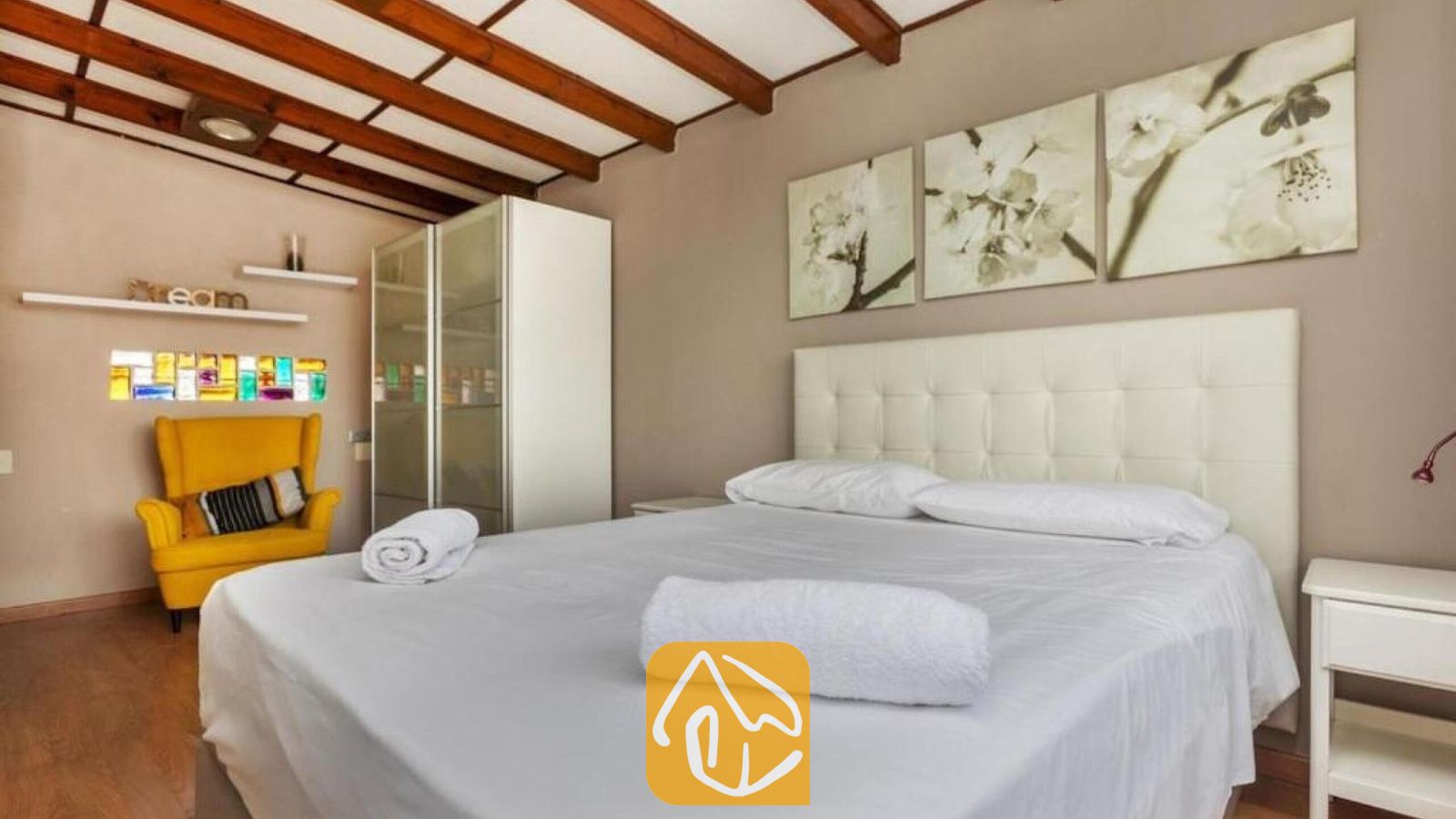 Vakantievilla's Costa Brava Spanje - Villa Soleia - Slaapkamer met een wit gecapitonneerd hoofdbord, houten balkenplafond en gele fauteuil bij Villa Soleia