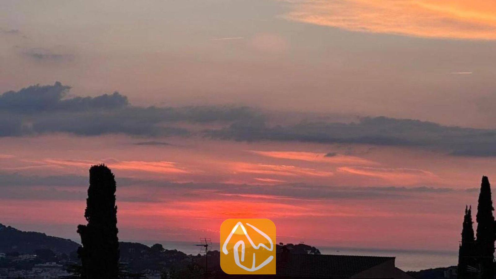 Vakantievilla's Costa Brava Spanje - Villa Soleia - Zonsondergang in tinten oranje en roze boven verre heuvels, gezien vanaf Villa Soleia met silhouetten van cipressen op de voorgrond.