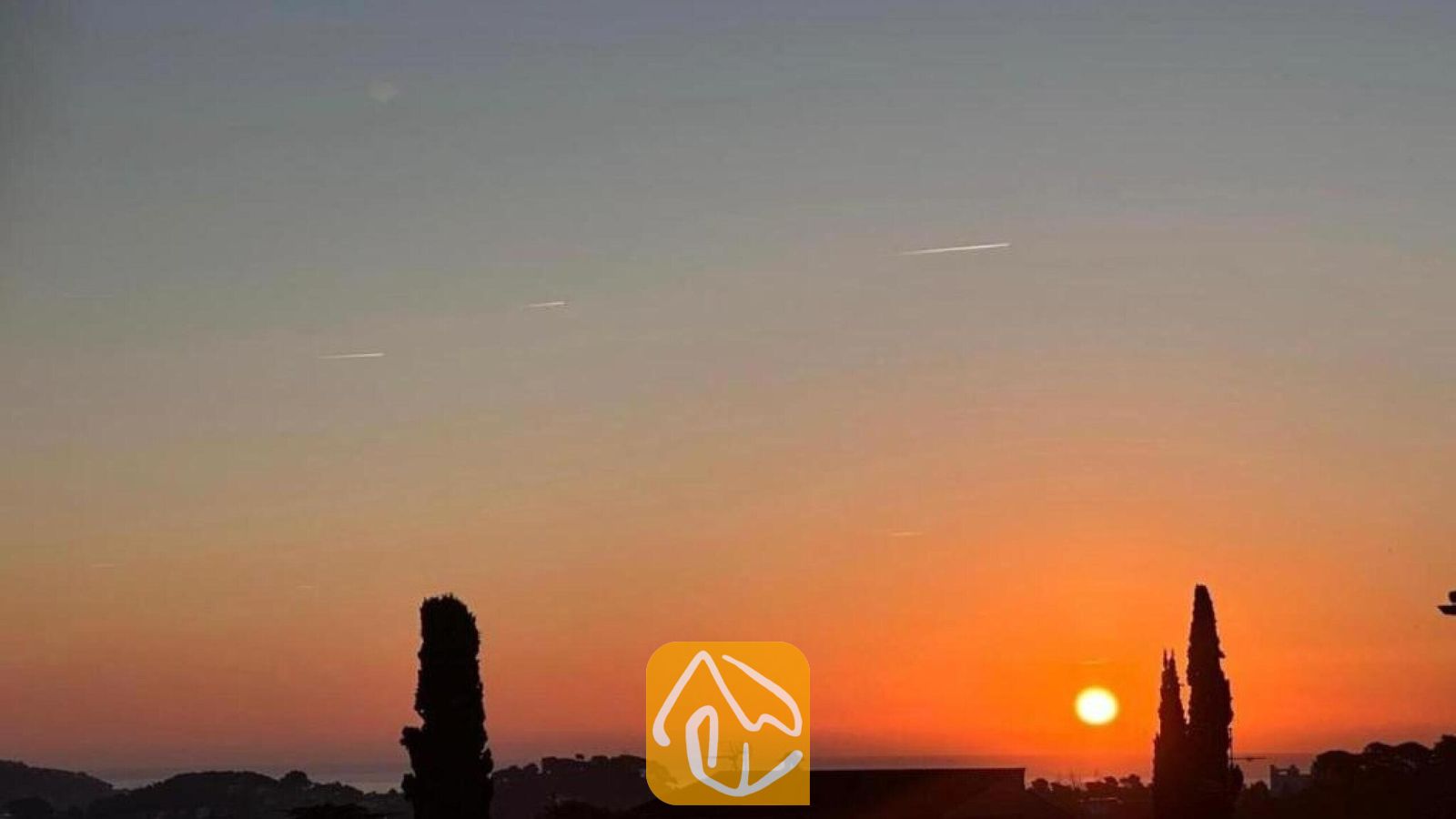 Vakantievilla's Costa Brava Spanje - Villa Soleia - Zonsondergang met levendige oranje en grijze gradiënten, gezien vanuit Villa Soleia, met silhouetten van cipressen en daken.