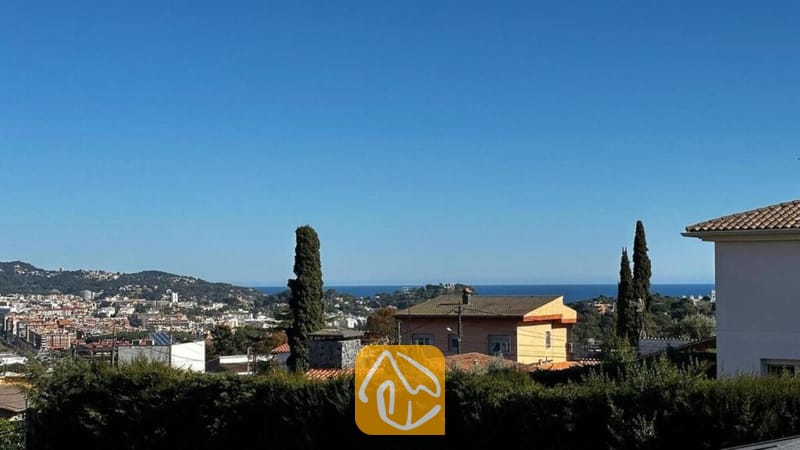 Villas de vacances Costa Brava Espagne - Villa Soleia - Vue en hauteur depuis la Villa Soleia montrant les bâtiments d'une ville au loin, des collines verdoyantes et un horizon marin bleu sous un ciel dégagé.
