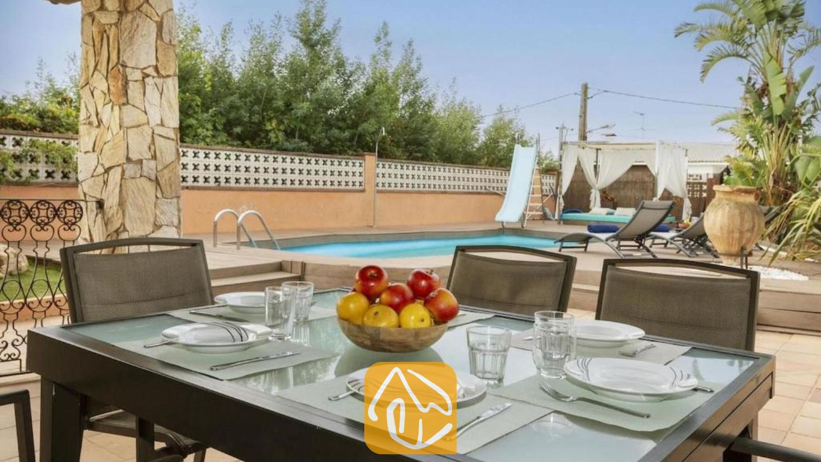 Vakantievilla's Costa Brava Spanje - Villa Soleia - Buiten eettafel met wit servies en een schaal met fruit bij Villa Soleia, met uitzicht op het privéprivate zwembad en de ligbedden.