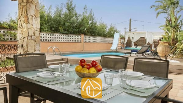 Vakantievilla's Costa Brava Spanje - Villa Soleia - Buiten eettafel met wit servies en een schaal met fruit bij Villa Soleia, met uitzicht op het privéprivate zwembad en de ligbedden.