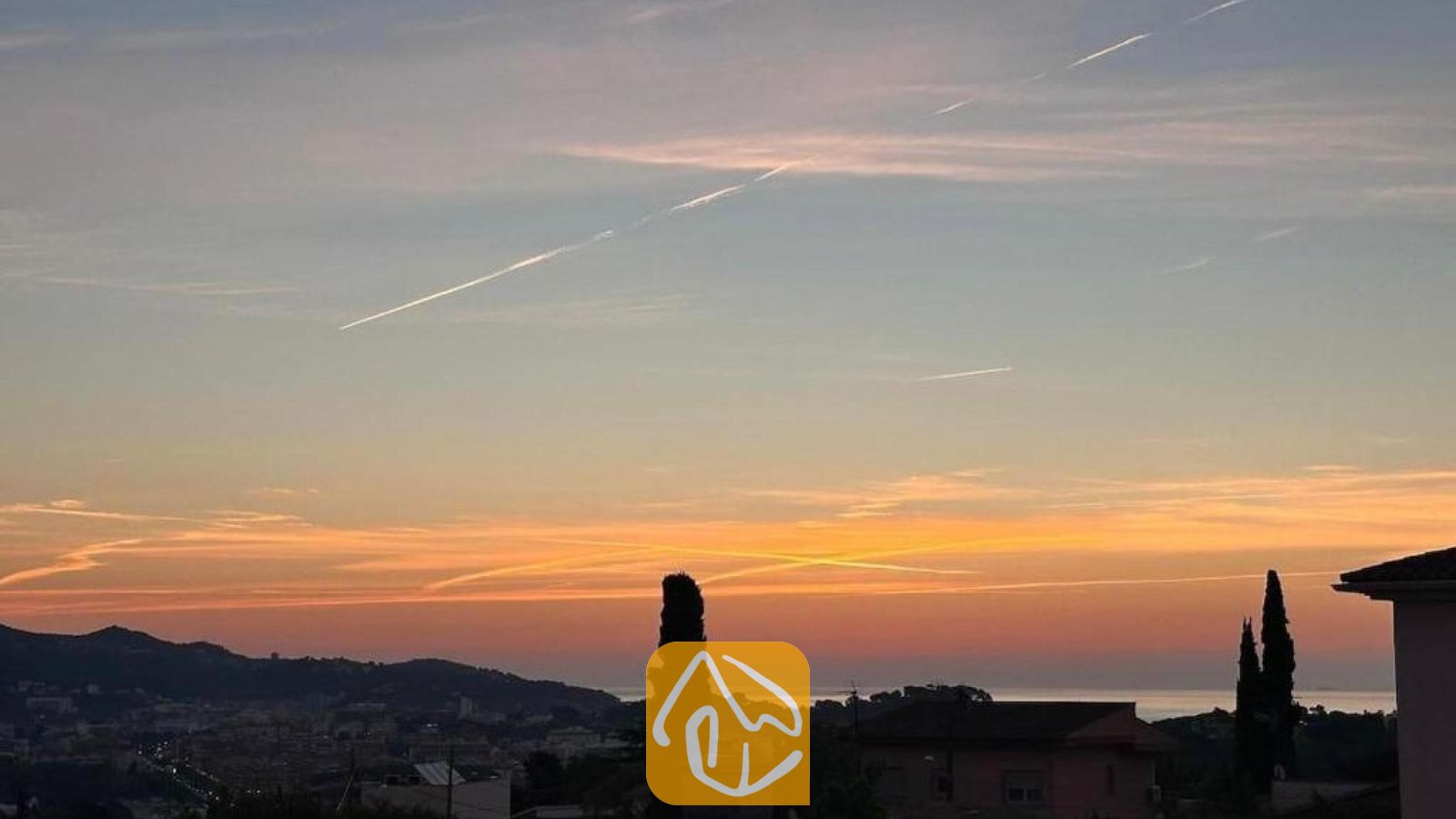 Vakantievilla's Costa Brava Spanje - Villa Soleia - Zonsondergang vanuit Villa Soleia in Spanje met uitzicht op verre heuvels, silhouetten van cipressen en een oranje met blauwe hemel vol vliegtuigstrepen.