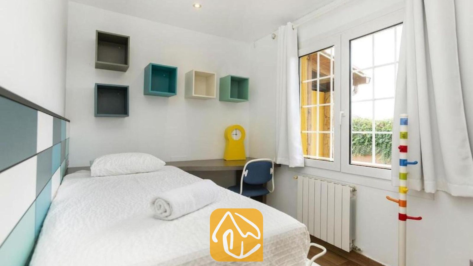 Vakantievilla's Costa Brava Spanje - Villa Soleia - Slaapkamer met een eenpersoonsbed, een klein bureau, blauwe en groene wandplanken en een raam met witte gordijnen.