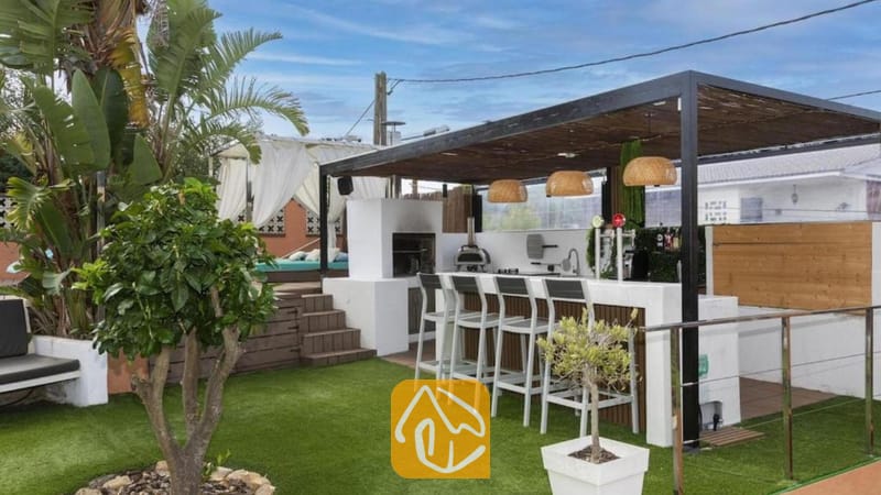 Vakantievilla's Costa Brava Spanje - Villa Soleia - Overdekte buitenbar bij Villa Soleia met hoge witte krukken, een ingebouwde grill, rieten hanglampen en kunstgras.