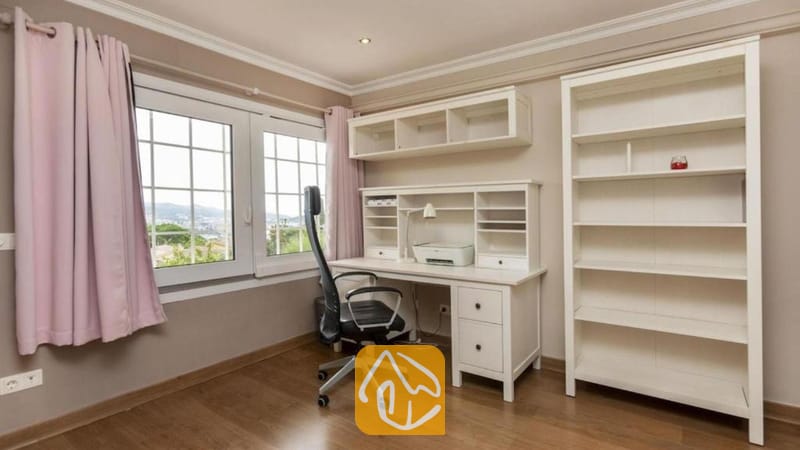 Villas de vacances Costa Brava Espagne - Villa Soleia - Espace bureau à domicile doté d'un bureau blanc, d'une grande bibliothèque, d'un fauteuil noir à roulettes et d'une fenêtre aux rideaux roses à la Villa Soleia.