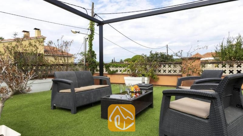 Vakantievilla's Costa Brava Spanje - Villa Soleia - Dakterras van Villa Soleia, voorzien van donkerkleurige rattan buitenmeubelen met beige kussens, een salontafel met glazen blad en kunstgras als vloerbedekking onder een metalen pergolaframe.
