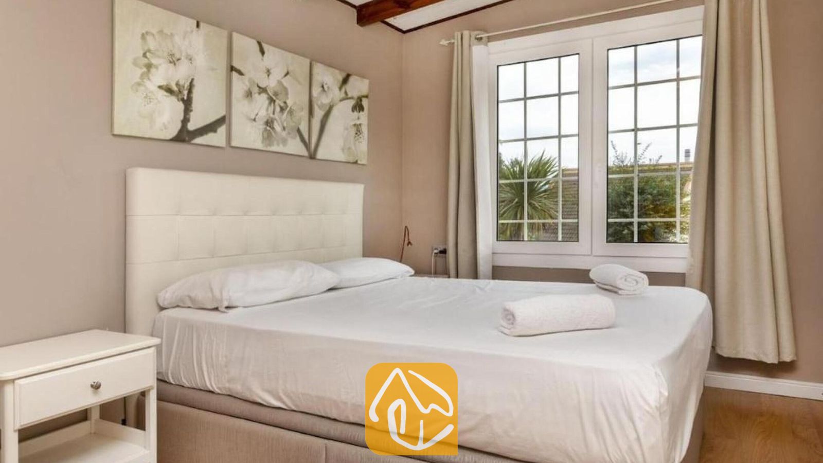 Vakantievilla's Costa Brava Spanje - Villa Soleia - Slaapkamer met een wit gestoffeerd hoofdeinde, opgevouwen handdoeken op het bed en een raam met beige gordijnen in Villa Soleia.