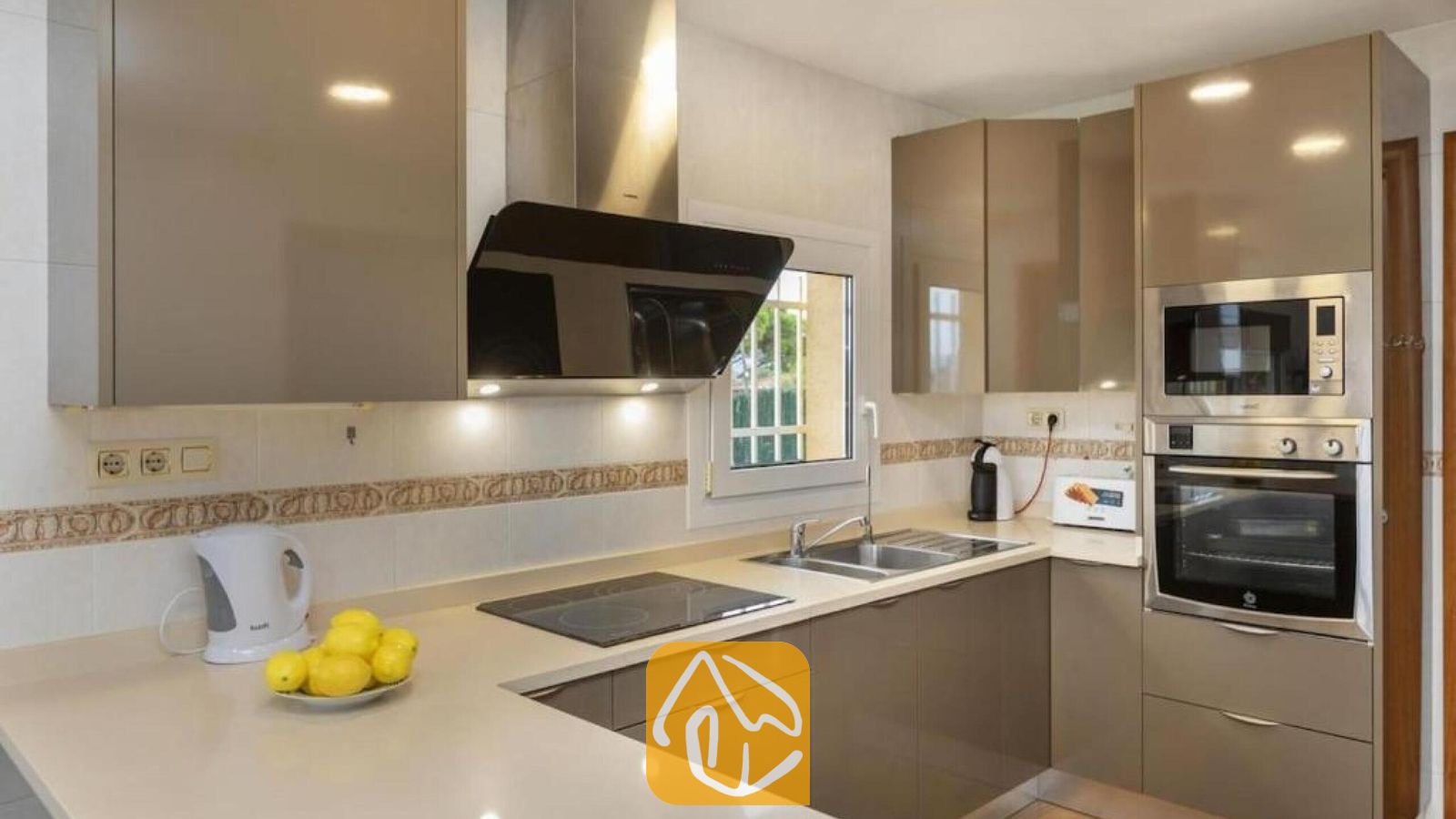 Vakantievilla's Costa Brava Spanje - Villa Soleia - Moderne keuken met hoogglans beige kasten, een roestvrijstalen inbouwoven en -magnetron, en een zwarte afzuigkap boven de kookplaat.