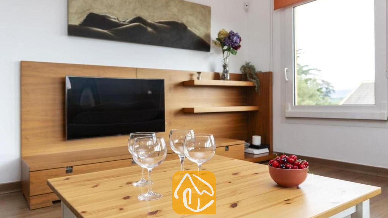 Vakantievilla's Costa Brava Spanje - Villa Soleia - Houten salontafel met wijnglazen en een schaal kersen in de woonkamer, voorzien van een aan de muur bevestigde tv en houten lambrisering.