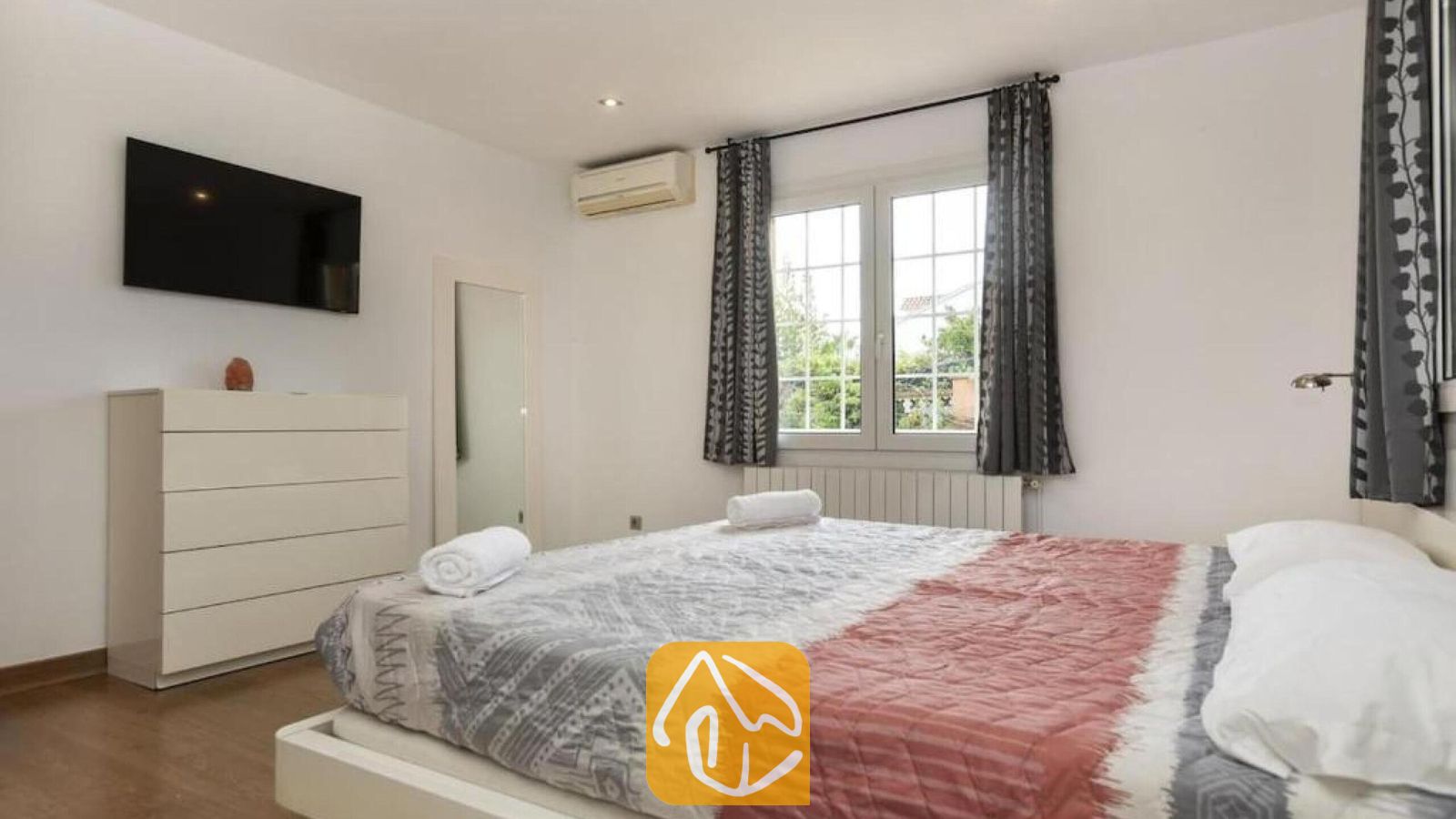 Vakantievilla's Costa Brava Spanje - Villa Soleia - Slaapkamer met een tweepersoonsbed voorzien van een rood-grijs patroonsprei, een witte ladekast, een wall-mounted televisie en een raam met grijs-gepatroneerde gordijnen.