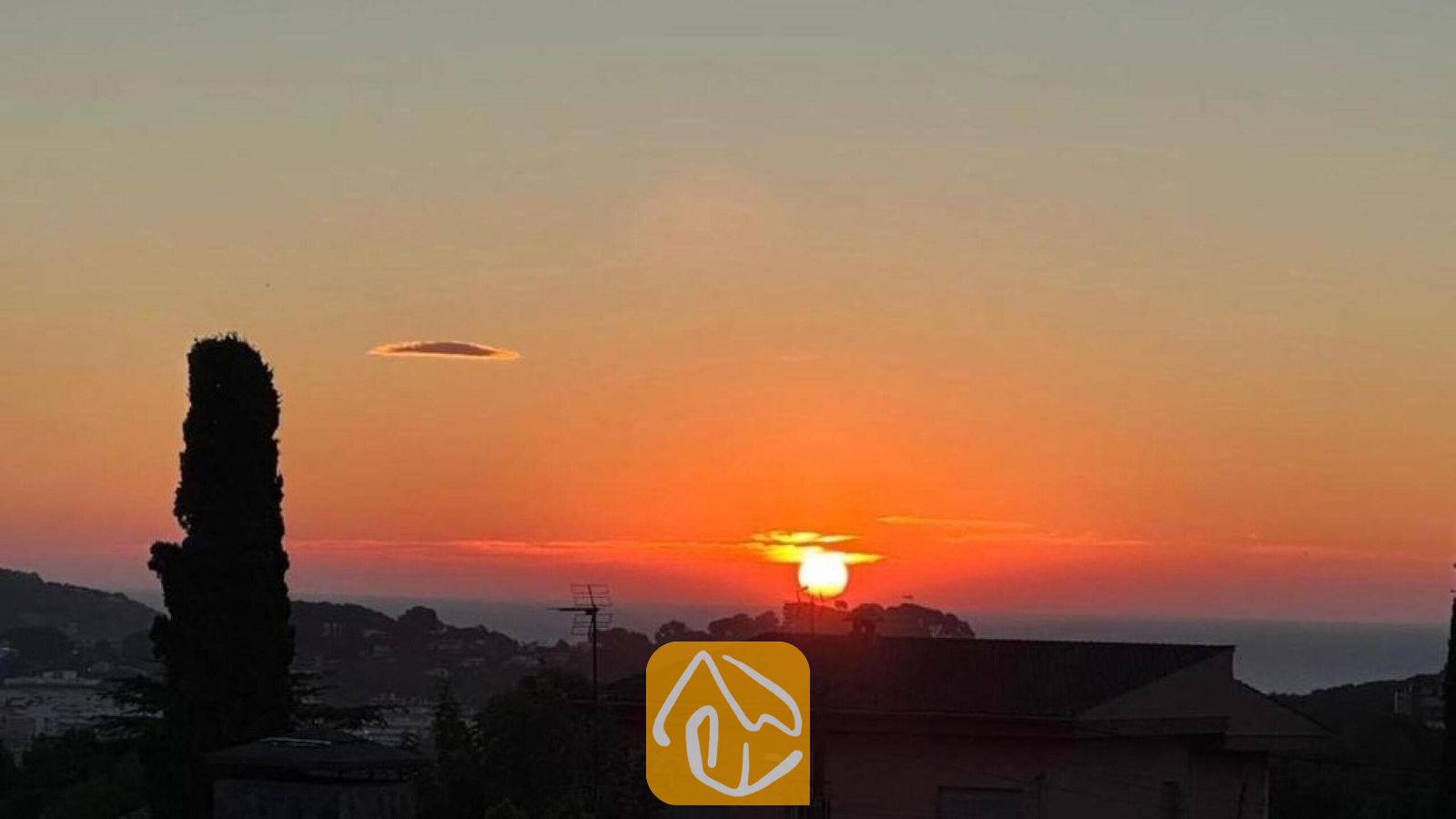 Vakantievilla's Costa Brava Spanje - Villa Soleia - Zonsondergang vanuit Villa Soleia, met een helderoranje lucht boven verre heuvels, het silhouet van een huisdak en een hoge cipres.