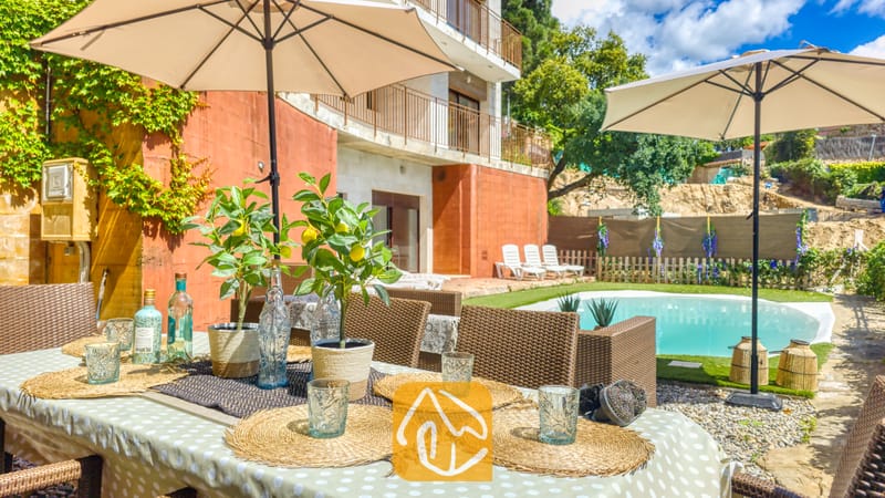 Vakantievilla's Costa Brava Spanje - Villa Sunny Beach - Buiten eettafel, gedekt met geweven placemats, glazen en potten met citroenplanten bij Villa Sunny Beach, met uitzicht op een zwembad en terras.