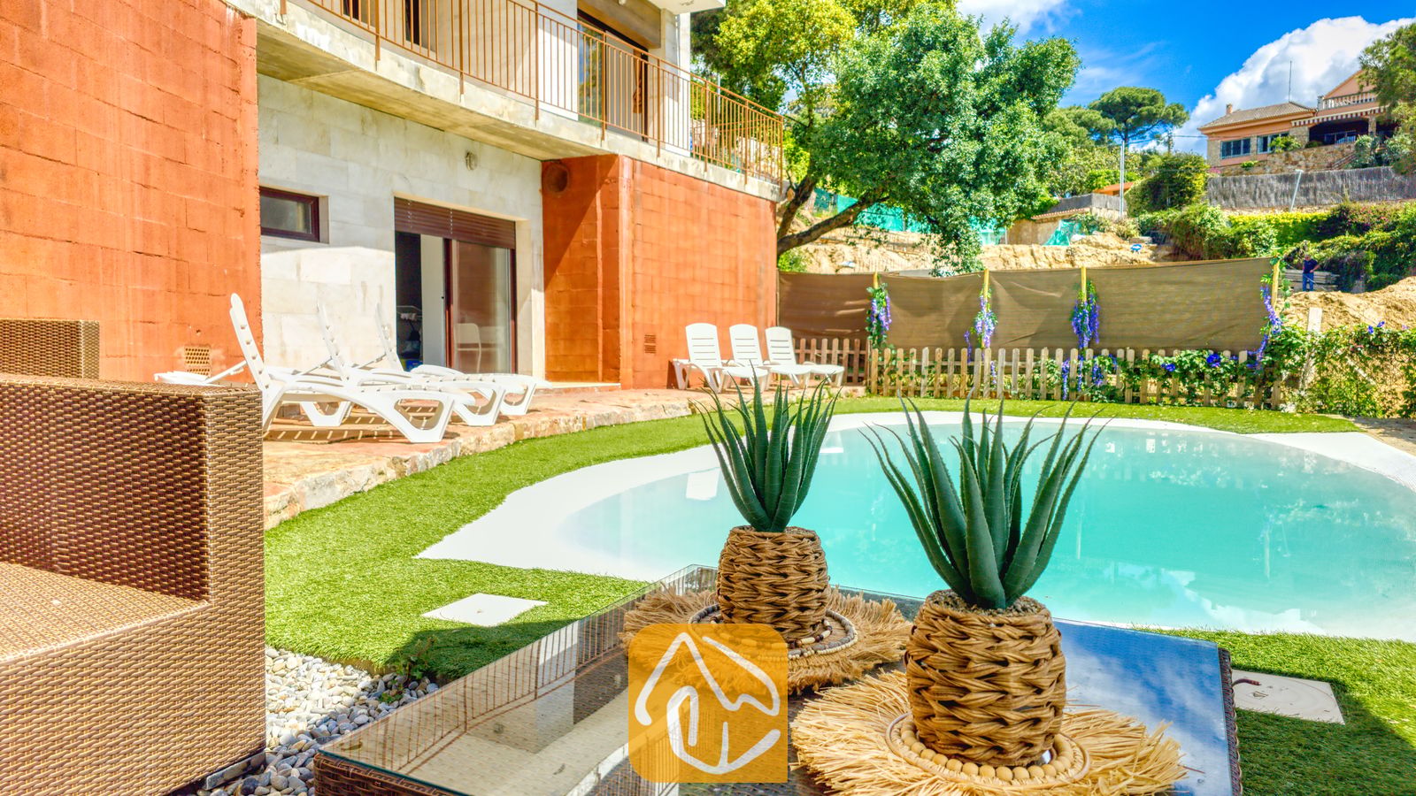 Vakantievilla's Costa Brava Spanje - Villa Sunny Beach - Privézwembad met een gebogen, blauw waterbassin, omringd door kunstgras, witte ligstoelen en terracotta buitenmuren bij Villa Sunny Beach.