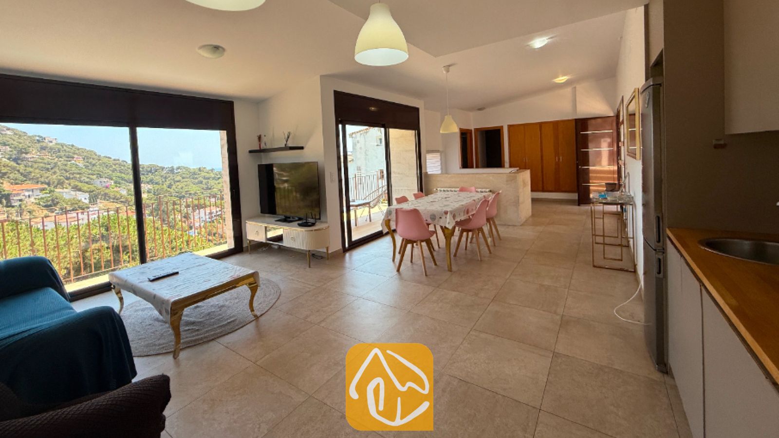 Vakantievilla's Costa Brava Spanje - Villa Sunny Beach - Open woon- en eetkamer in Villa Sunny Beach met tegelvloeren, grote glazen schuifdeuren en roze eetkamerstoelen.